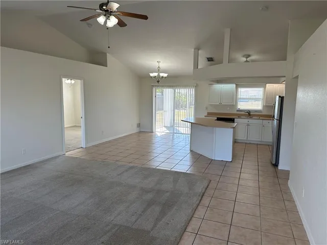 Kitchen featuring light tile patterned floors, high vaulted ceiling, stainless steel fridge, pendant lighting, and white cabinets
