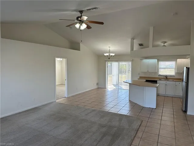 Kitchen with stainless steel appliances, sink, light tile patterned floors, white cabinets, and a kitchen island