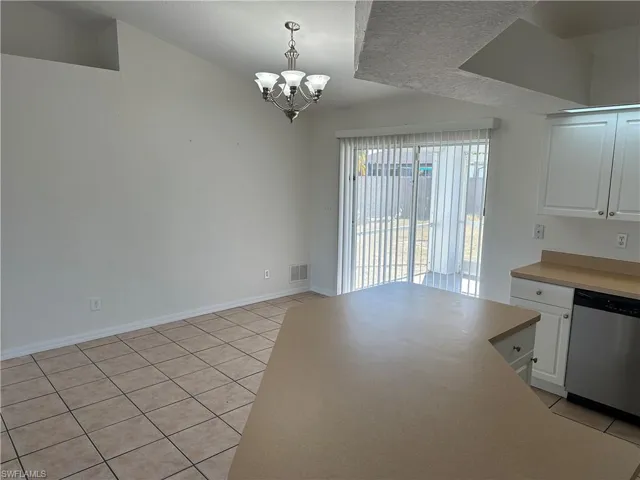 Unfurnished dining area featuring light tile patterned floors, a textured ceiling, and an inviting chandelier