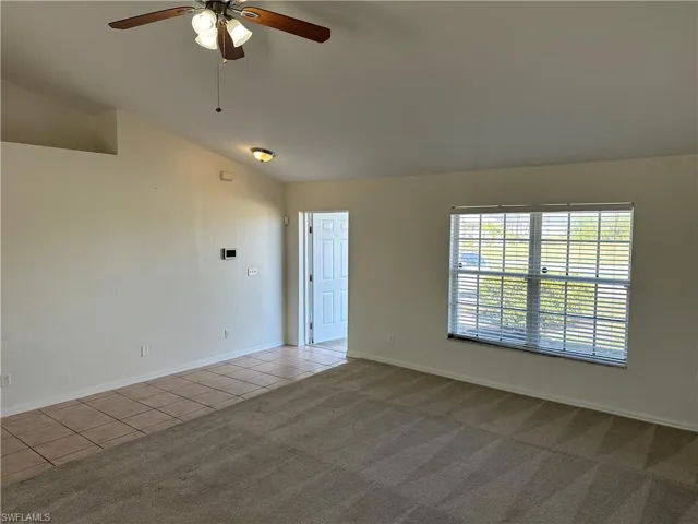Carpeted empty room with ceiling fan and lofted ceiling