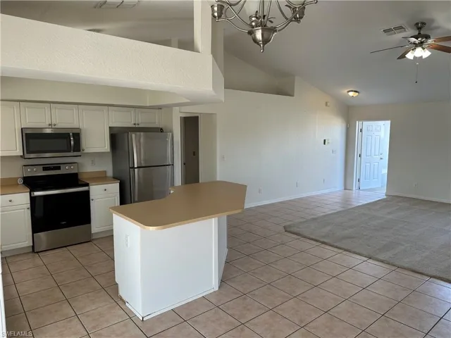Kitchen featuring ceiling fan with notable chandelier, light tile patterned floors, appliances with stainless steel finishes, decorative light fixtures, and white cabinetry