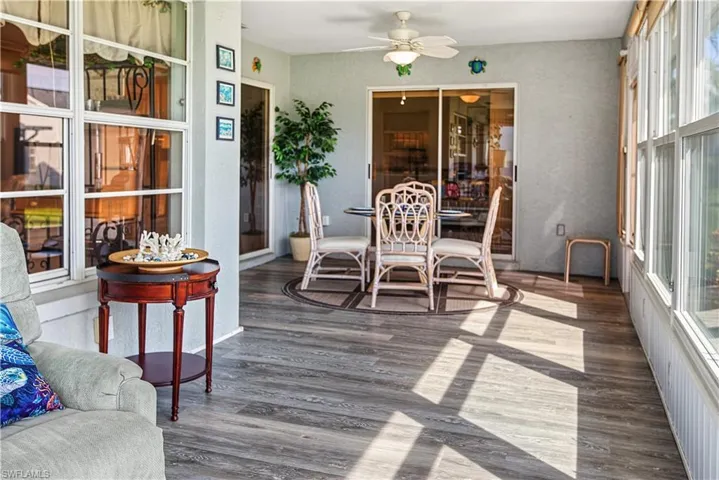 Enclosed patio with wood-finish flooring, white ceiling fan, and large windows