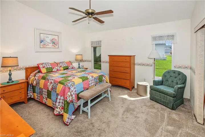 Vaulted ceiling with a ceiling fan, two windows, carpeted flooring, and white walls