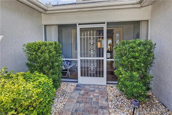 Paver walkway leading to a screened entryway with decorative security door, surrounded by established landscaping and gravel beds