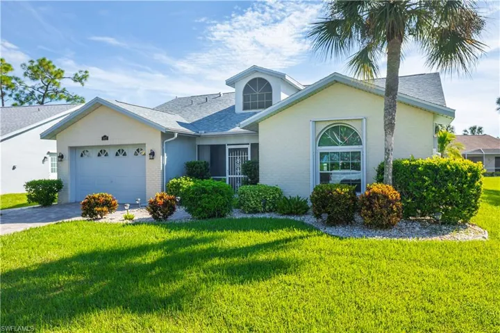 Stucco exterior with a gabled roof, arched window, attached garage, and established landscaping