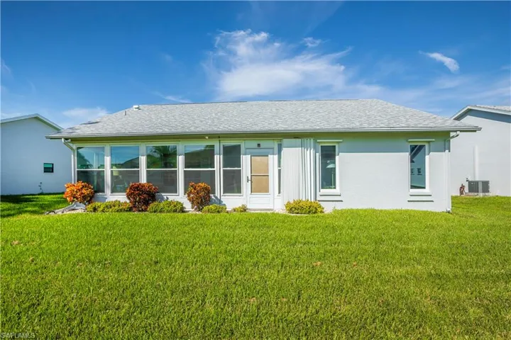 Expansive rear lawn, full-width sunroom with multiple windows, stucco exterior, and a shingle roof