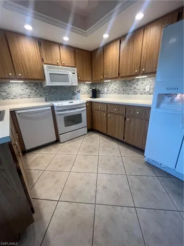 Recessed lighting, wood-finish cabinetry, tile flooring, mosaic tile backsplash, and white appliances