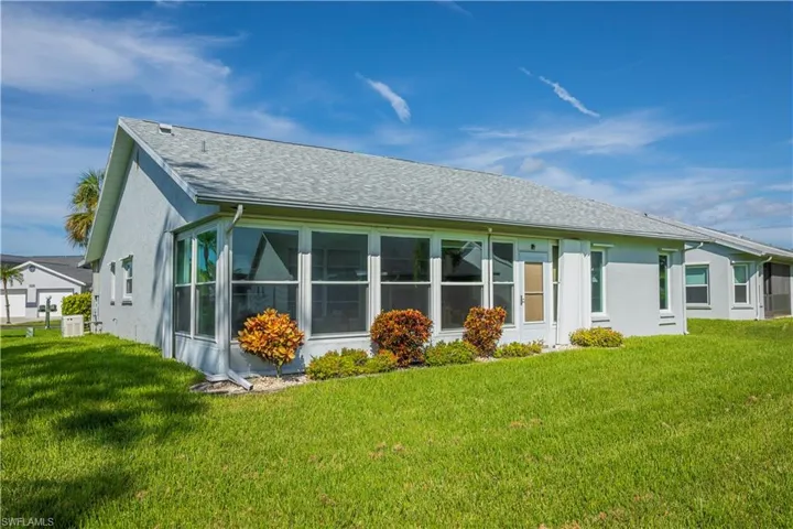 Expansive green lawn bordering the stucco exterior, featuring a white-framed sunroom with multiple windows, and a light gray shingle roof
