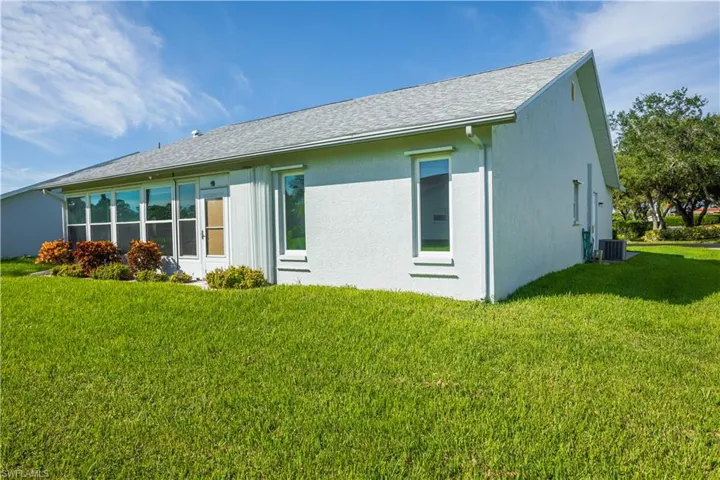 Stucco exterior with a pitched shingle roof, multiple windows, and an air conditioning unit