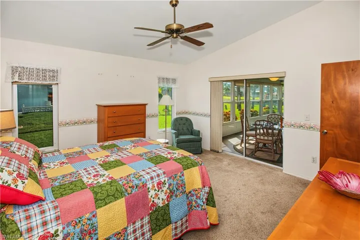 Spacious primary bedroom suite featuring neutral carpeting, ceiling fan with integrated lighting, wood-finish dresser, glass sliding doors opening to outdoor patio access, and abundant natural light from multiple windows