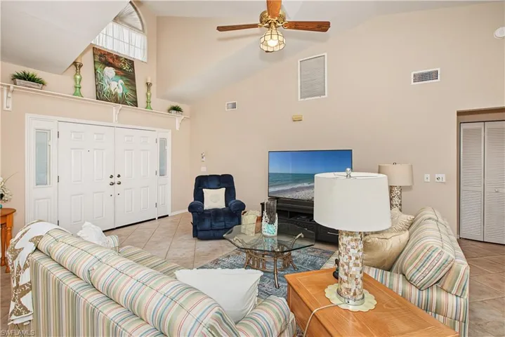Vaulted ceiling with an arched transom window, double-panel entry doors with sidelights, a ceiling fan, and tile flooring