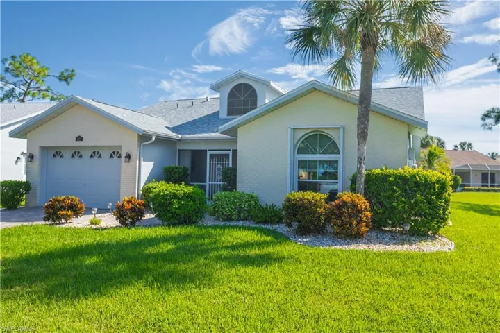 Stucco exterior featuring an arched window, a dormer, an attached garage, and landscaping with a palm tree