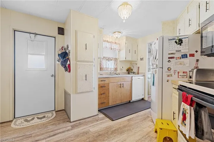 Kitchen with stainless steel electric range oven, a chandelier, light countertops, light wood-style floors, and white dishwasher