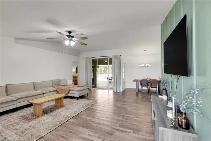 Living room with vaulted ceiling, durable laminate floors, a ceiling fan, and hanging lights