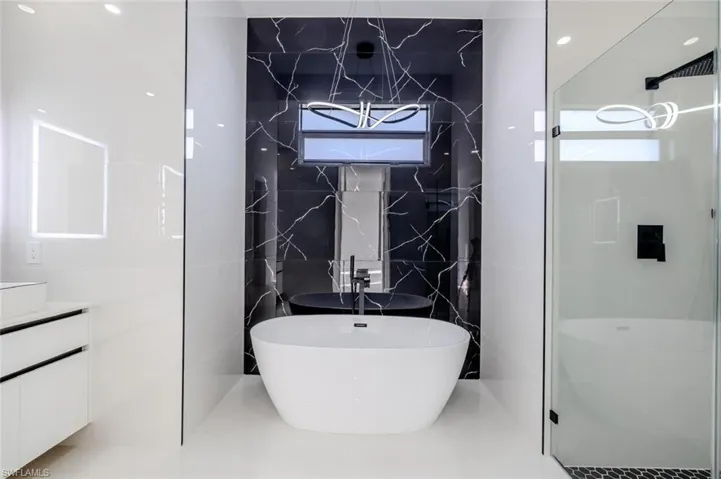 Bathroom with a soaking tub, a stall shower, vanity, and tile walls