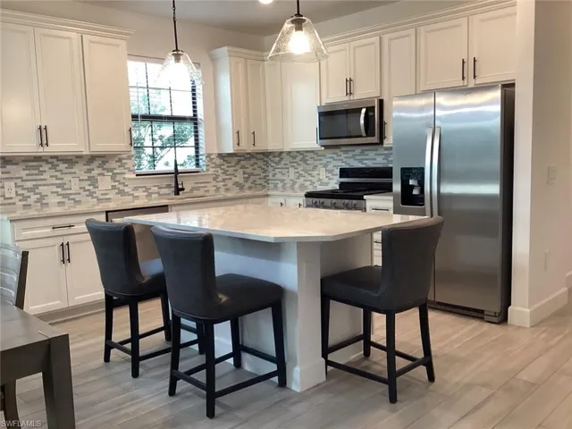 Kitchen with stainless steel appliances, decorative light fixtures, a kitchen bar, a kitchen island, and white cabinets
