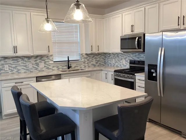 Kitchen featuring stainless steel appliances, a center island, pendant lighting, light stone countertops, and decorative backsplash