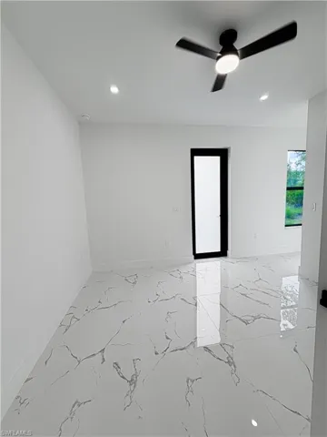 Spacious room featuring large format tile flooring with distinctive veining, a modern ceiling fan with integrated lighting, recessed lighting, and a contemporary door with a frosted glass panel