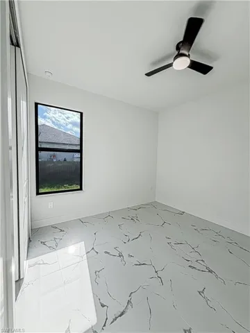 Spacious room featuring large format tile flooring with a marble-effect pattern, a contemporary ceiling fan with integrated lighting, and a window providing natural illumination