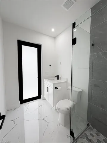 Modern bathroom featuring white walls, large format white tile flooring with gray veining, and a clear glass shower enclosure