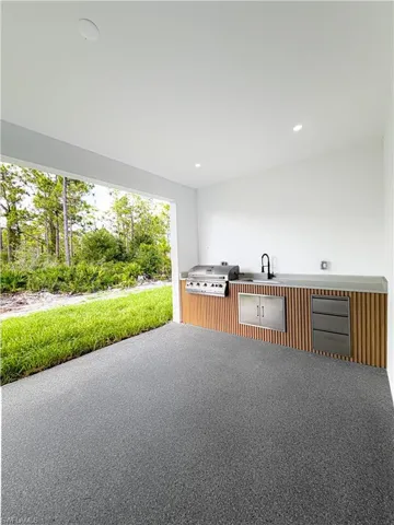Covered outdoor kitchen featuring a built-in grill, integrated sink with a black faucet, and stainless steel cabinetry