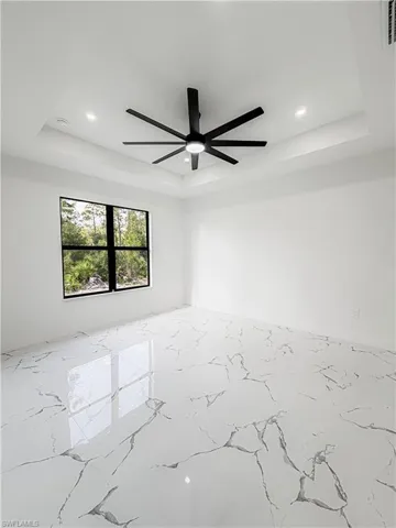 Spacious room featuring a tray ceiling with recessed lighting, a modern black ceiling fan, and large format polished tile flooring