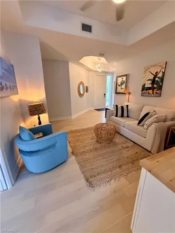 Living area with a raised ceiling, light wood-style flooring, ceiling fan, and arched walkways