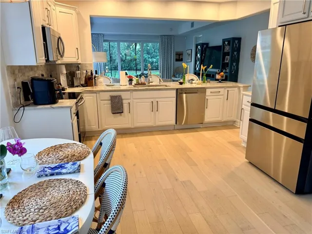 Kitchen featuring stainless steel appliances, white cabinets, light wood-style floors, and light stone counters