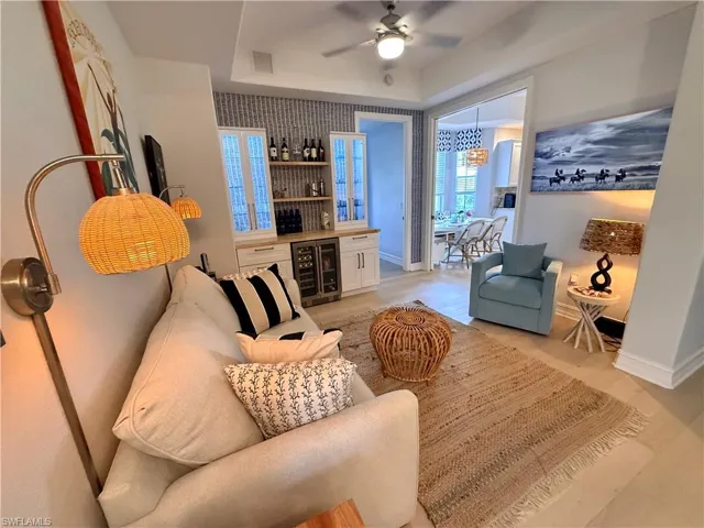 Living area featuring a bar, wine cooler, a ceiling fan, a raised ceiling, and light wood-style floors