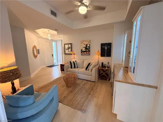 Living area featuring light wood finished floors, a raised ceiling, and a ceiling fan