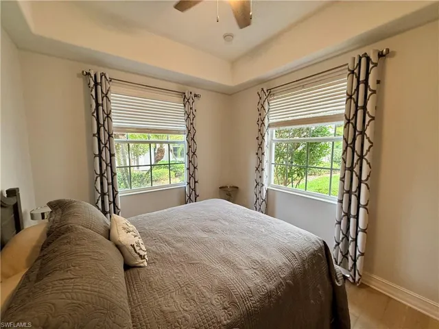 Bedroom with multiple windows, a tray ceiling, a ceiling fan, and wood finished floors