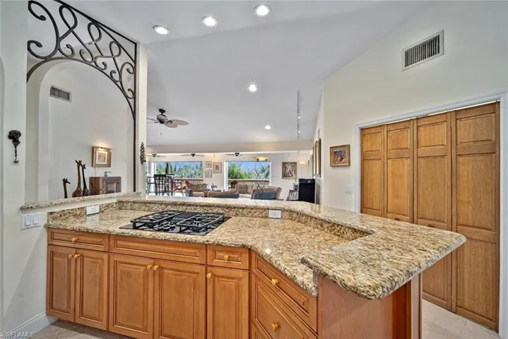 Kitchen featuring brown cabinetry, light stone countertops, recessed lighting, open floor plan, and lofted ceiling