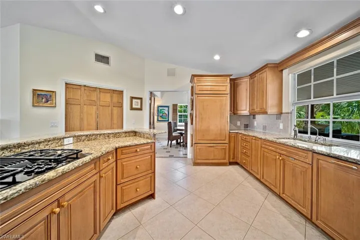 Kitchen with vaulted ceiling, light stone counters, brown cabinets, light tile patterned flooring, and recessed lighting