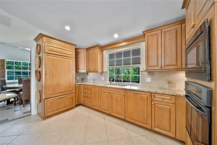 Kitchen with light stone countertops, light tile patterned floors, black appliances, backsplash, and recessed lighting
