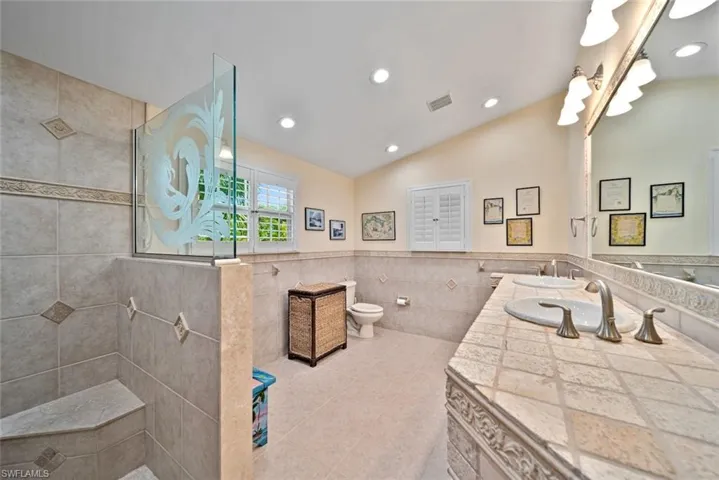 Bathroom featuring tile walls, walk in shower, double vanity, light tile patterned flooring, and a wainscoted wall