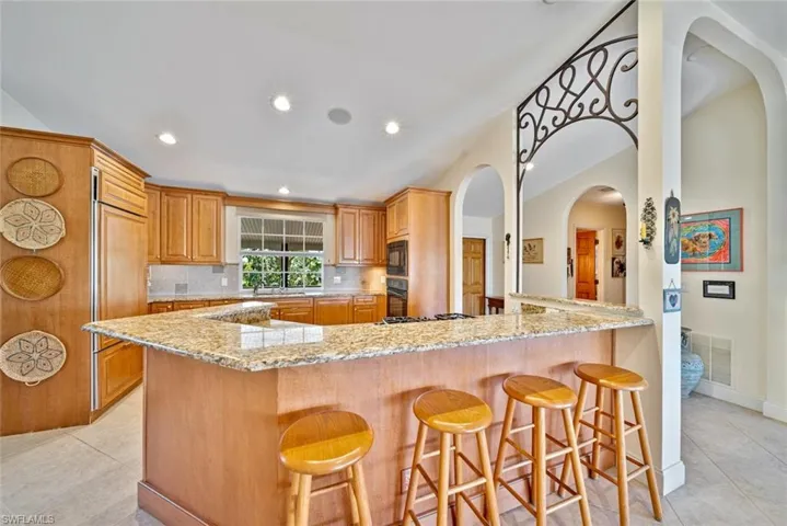 Kitchen with light tile patterned floors, a breakfast bar area, light stone countertops, decorative backsplash, and recessed lighting