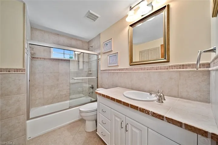 Full bath with tile walls, vanity, bath / shower combo with glass door, light tile patterned floors, and a wainscoted wall