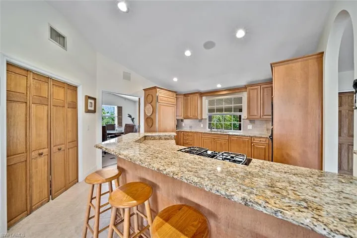 Kitchen featuring recessed lighting, a breakfast bar area, decorative backsplash, light stone countertops, and light tile patterned flooring
