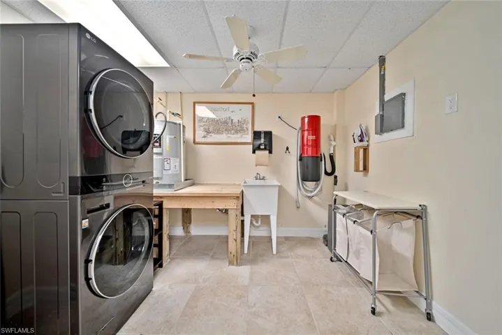 Laundry area featuring a drop ceiling, stacked washer and clothes dryer, ceiling fan, electric water heater, and light tile patterned floors