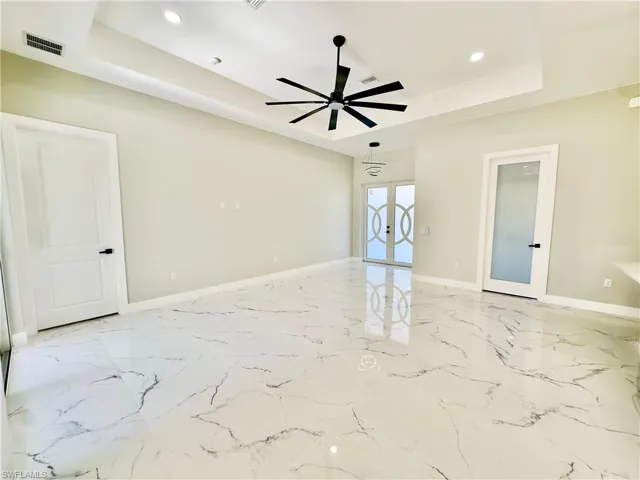 Unfurnished room featuring a tray ceiling, french doors, recessed lighting, light marble finish flooring, and ceiling fan