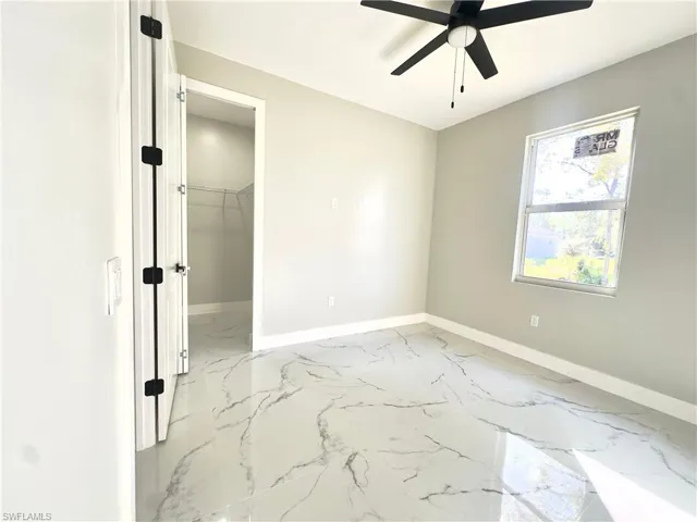 Unfurnished bedroom featuring light marble finish flooring, a walk in closet, and ceiling fan