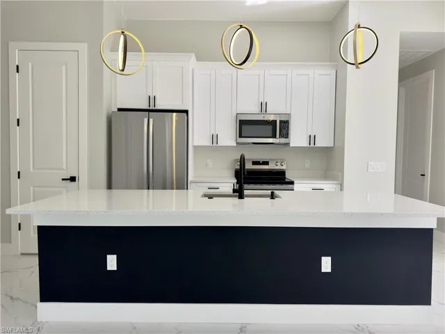 Kitchen with appliances with stainless steel finishes, white cabinets, light stone counters, and an island with sink