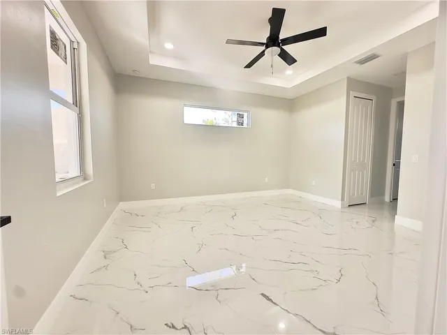 Empty room featuring light marble finish floors, recessed lighting, a tray ceiling, and a ceiling fan