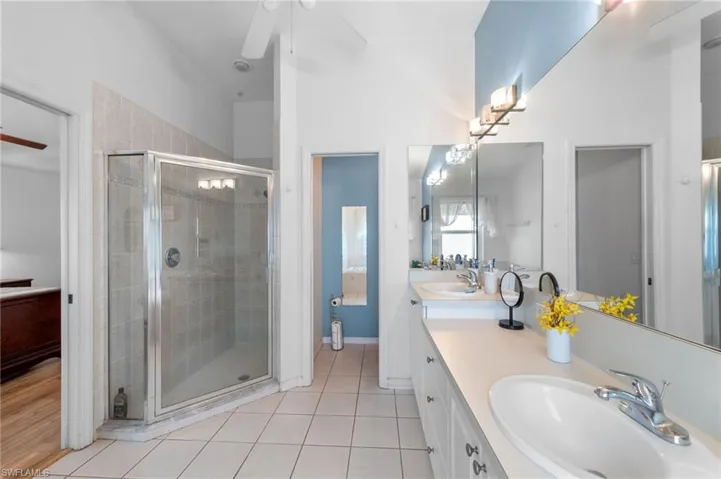 Bathroom featuring double vanity, a stall shower, a ceiling fan, and tile patterned flooring