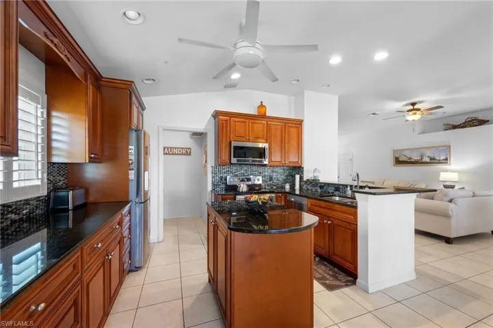 Kitchen with appliances with stainless steel finishes, ceiling fan, open floor plan, backsplash, and a peninsula