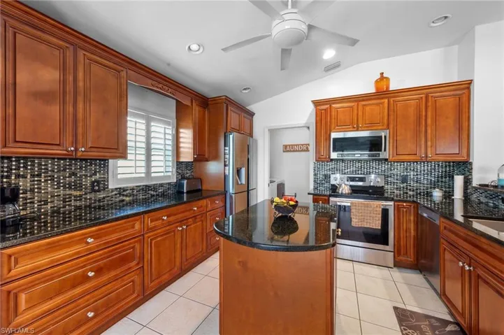 Kitchen featuring appliances with stainless steel finishes, lofted ceiling, a ceiling fan, a kitchen island, and decorative backsplash