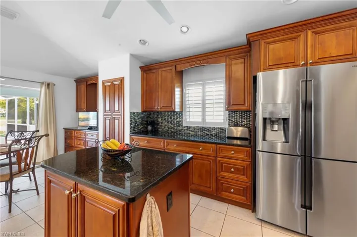 Kitchen featuring stainless steel refrigerator with ice dispenser, light tile patterned floors, decorative backsplash, brown cabinetry, and recessed lighting