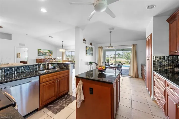 Kitchen with stainless steel dishwasher, vaulted ceiling, ceiling fan, light tile patterned floors, and dark stone countertops
