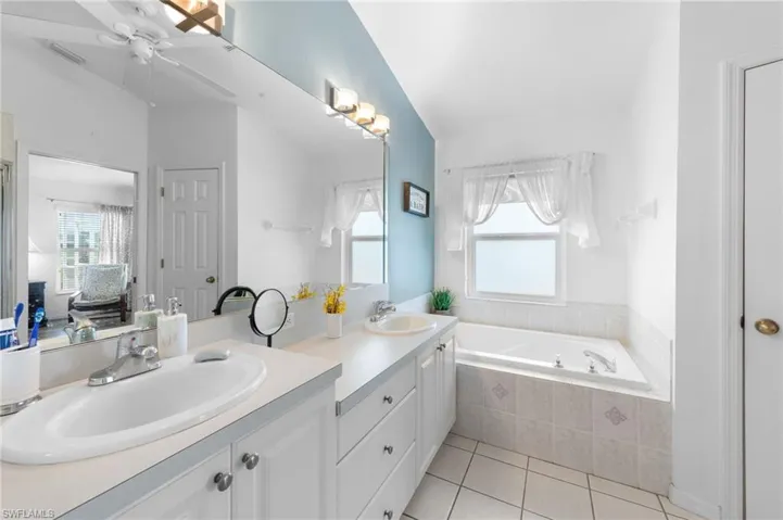 Full bath with tile patterned flooring, double vanity, a bath, and plenty of natural light