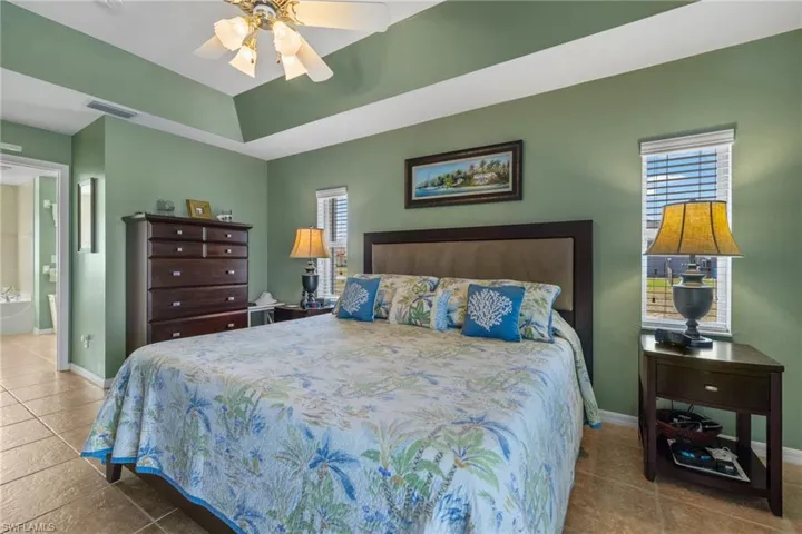 Bedroom with multiple windows, a raised ceiling, ensuite bathroom, and tile patterned floors